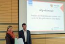 Amtsleiter Christian Kreye und Landrätin Baier-Müller stehen vor der Powerpointpräsentation zum AllgaEumobil. 