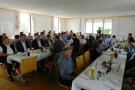 Blick in den Saal des Bürger- und Vereinsheims, wo Menschen an Tischen sitzen.