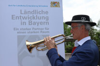 Ein Musiker mit Hut bläst in ein Flügelhorn. Er steht vor einem Rollup mit der Aufschrift „Ländliche Entwicklung in Bayern“.