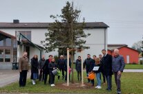 Kinder, Frauen und Männer stehen um die neue Dorflinde im Schulhof von Ellgau