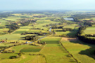Luftaufnahme mit Blick ins GünztaL Eingebettete Dörfer, die Konturen von Wiesen und Äckern, der Fluss Günz und im Hintergrund ein Stausee. 