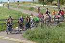 Radlgruppe mit Kindern und Erwachsenen überqueren eine Brücke auf geteertem Radweg. 