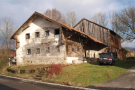 Ein niederbayerisches Waldlerhaus in seiner alten Form. Im Hintergrund ist eine marode Scheune ersichtlich.