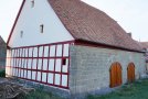 Sanierte landwirtschaftliche Scheune aus Sandstein mit neuer Biberschwanzdeckung, rotem Fachwerk und zwei neuen Holztoren