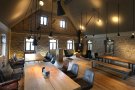 Innenansicht eines freien, großzügigen Dachraums mit Natursteinwänden als moderne Weinprobierstube mit langen Holztischen und schwarzen Ledersesseln eingerichtet