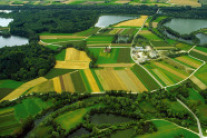 Landwirtschaftliche Nutzfläche umgeben von Seen, Wald und einem mäandrierenden Bach
