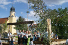 Dorfplatzsituation: Junge Frauen und Männer führen auf einem Podium einen Tanz auf. Im Hintergrund steht Kirche.